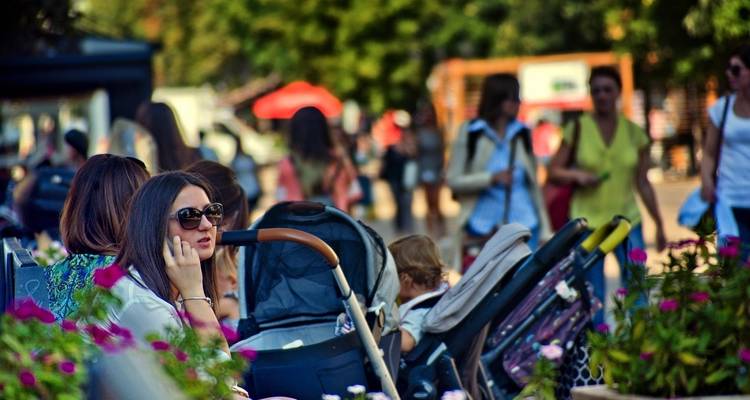 People sitting outdoors in a bustling park area with flowers and trees.