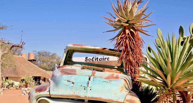 Een oude auto met een bord waarop 'Solitaire' staat, omringd door cactussen.