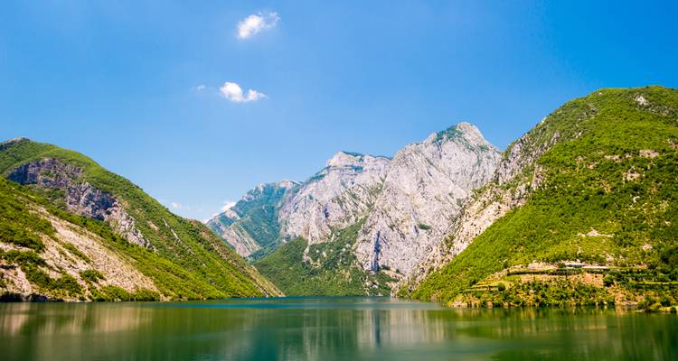 Kristallklarer See umgeben von dramatischen grünen Bergen und felsigen Klippen unter einem strahlend blauen Himmel