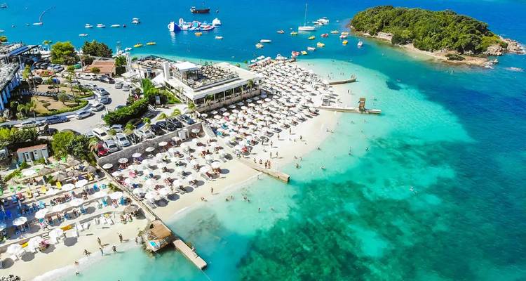 Complejo turístico de playa bullicioso en Ksamil con sombrillas y agua cristalina.