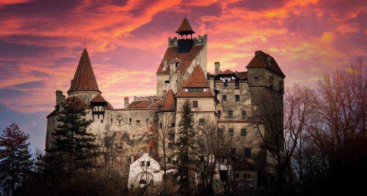 Château de Bran au coucher du soleil avec un ciel dramatique.