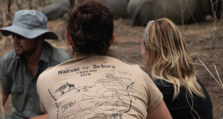 Des gens assis près d'un rhinocéros, l'un portant un t-shirt avec une carte.