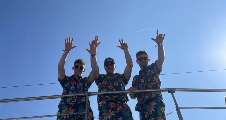 Trois hommes en tenues florales assorties qui saluent de la main sur un bateau.