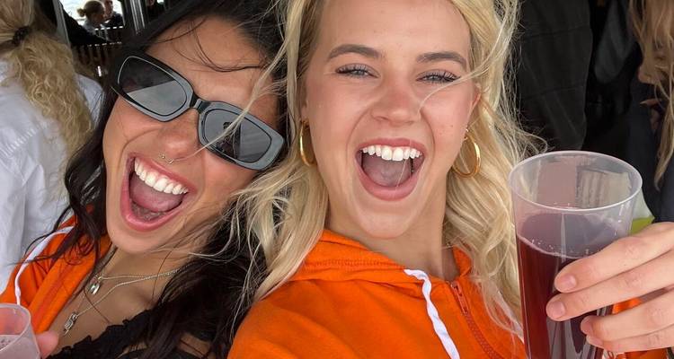 Deux femmes souriant largement avec des boissons sur un bateau.