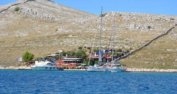 Yachts docked near a hillside with stone buildings.
