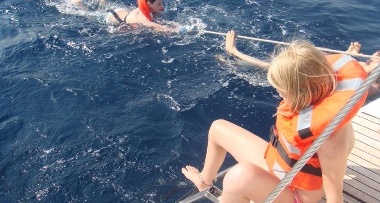 Children with life jackets swimming near a boat.