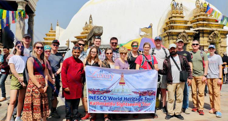 Grupo de turistas sosteniendo una pancarta de tour frente a una estupa.