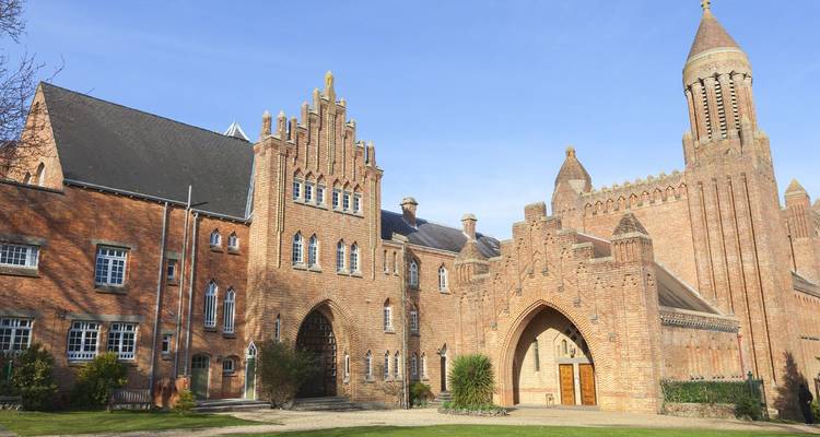 Bâtiment de style abbaye en brique avec une haute tour sous un ciel bleu dégagé