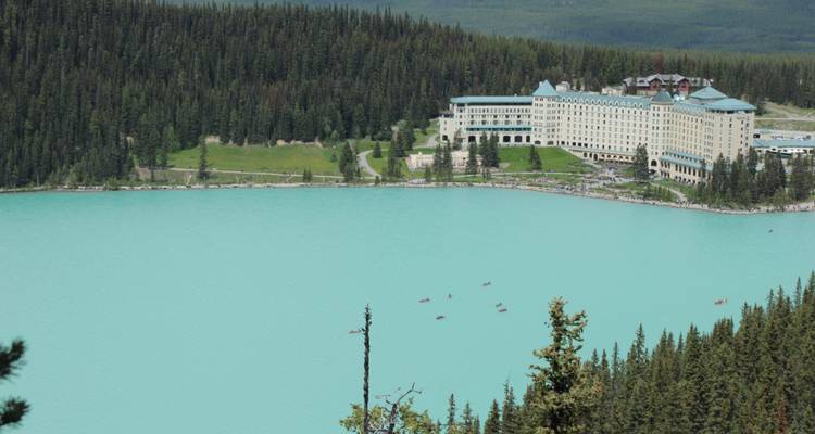 Hotel de lujo junto a un lago turquesa rodeado de bosque.