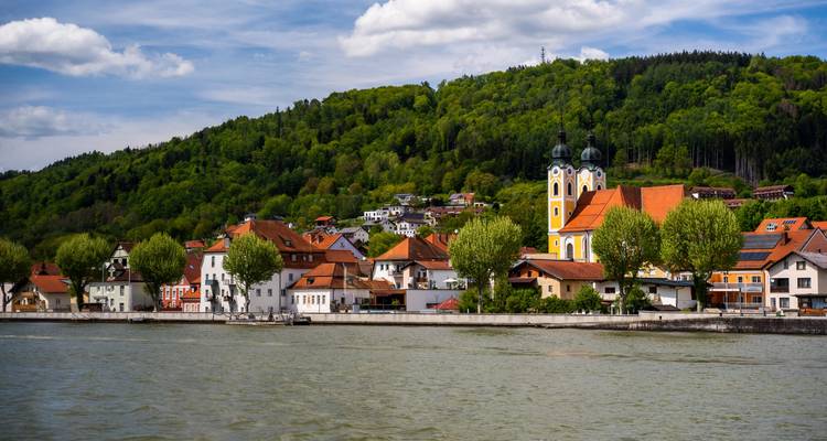 Bonito pueblo ribereño con iglesia barroca de torres gemelas y fondo de ladera boscosa