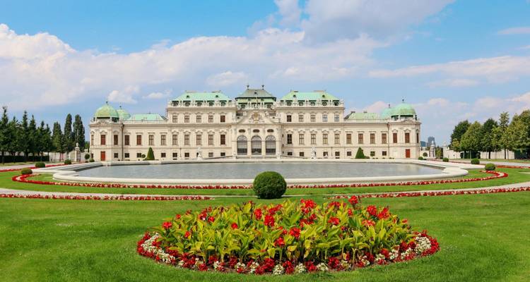 Palacio Belvedere con un parterre circular de flores y un extenso césped en primer plano en un día luminoso