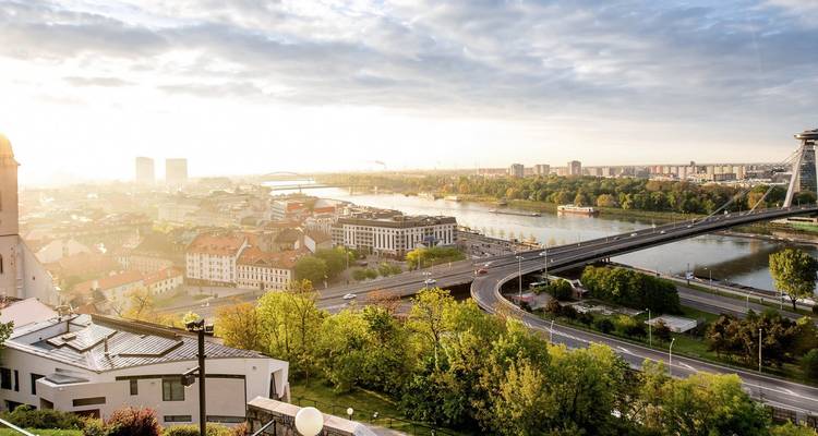 Amplio paisaje urbano de Bratislava con río, puentes y cielo brillante.
