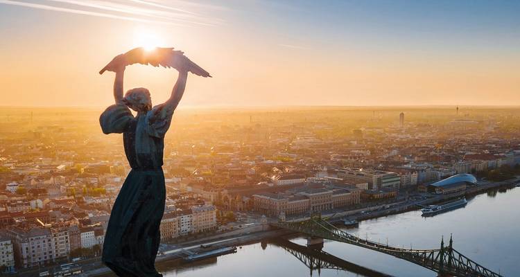 Lever de soleil doré derrière la Statue de la Liberté de Budapest surplombant le Danube et le paysage urbain