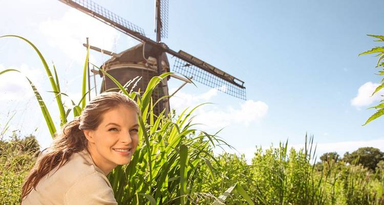 Femme souriante accroupie parmi les hautes herbes avec un moulin à vent hollandais classique derrière elle par une journée ensoleillée
