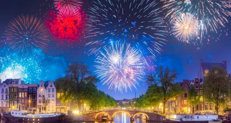Feux d'artifice brillants éclatant au-dessus d'un canal illuminé et de maisons hollandaises historiques la nuit.
