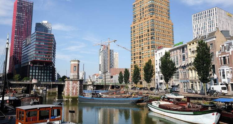 Horizonte moderno de Róterdam with torres coloridas, grúas y barcazas atracadas a lo largo de un canal en un día despejado.