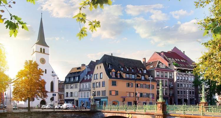 Edificios ribereños pintados de colores brillantes y campanario de iglesia en Estrasburgo bañados en suave luz de tarde.