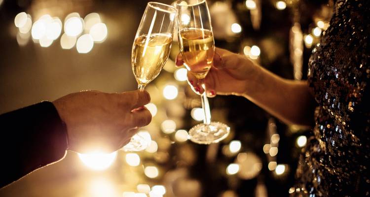 Primer plano de dos manos brindando con copas de champán contra luces festivas difuminadas