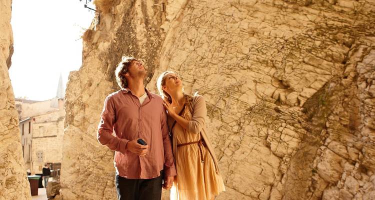 Ein Paar hält Händchen und blickt zu den hoch aufragenden Steinmauern in einer sonnenbeschienenen Gasse empor.
