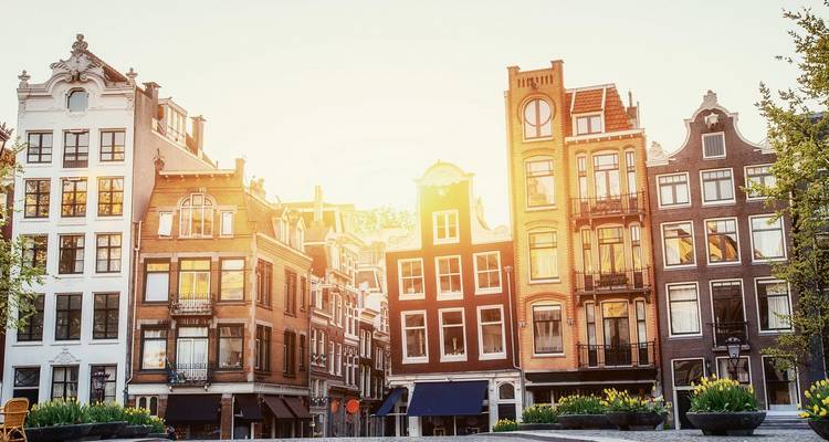 Row of classic narrow Amsterdam canal houses glowing in warm sunset light.