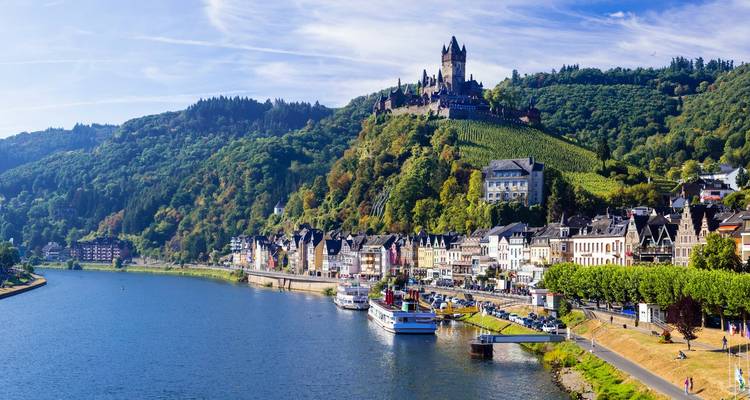 Picturesque riverside town of Cochem with colourful houses, vineyards and Reichsburg Castle perched on a forested hill above the Moselle River.