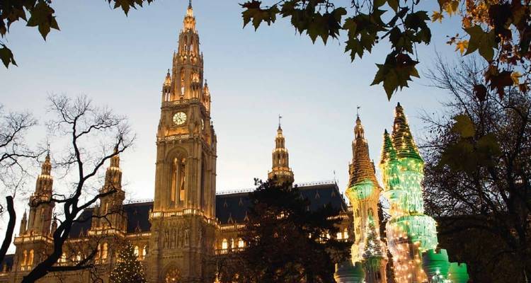 Hôtel de ville de Vienne encadré par des feuilles d'automne et des illuminations de fête au crépuscule.