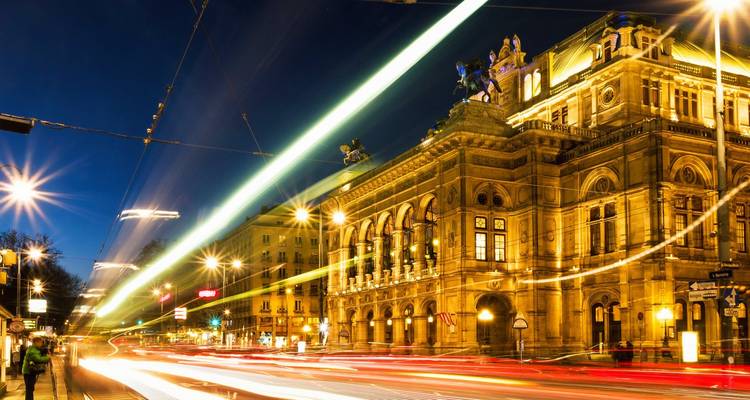 Des traînées lumineuses de tramways filent devant la façade grandiose de l'Opéra d'État de Vienne au crépuscule.