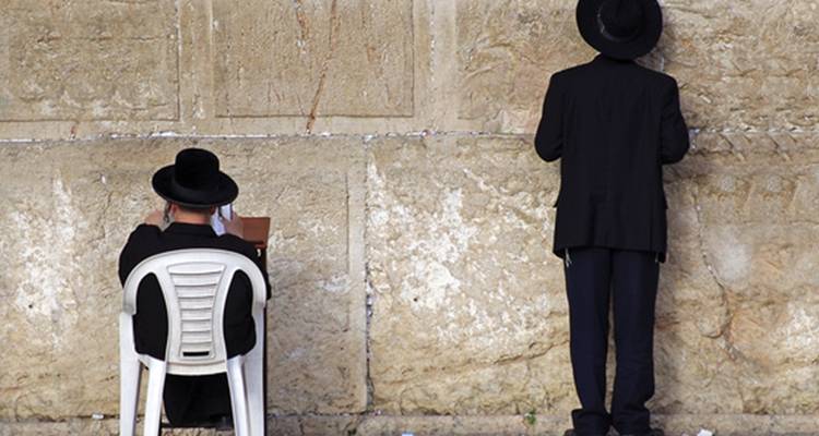 Religious men praying at a historic stone wall.