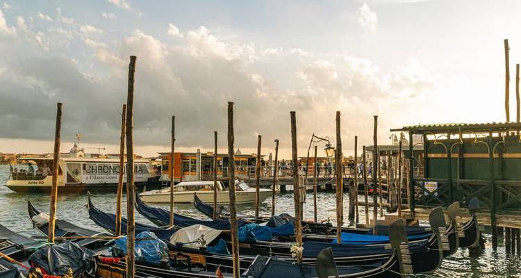 Eine Reihe von Gondeln schaukelt neben hölzernen Pfählen bei Sonnenuntergang mit dramatischen Wolken über der venezianischen Lagune.