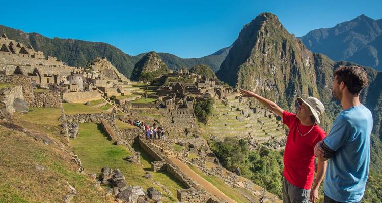 Guide pointing out ruins to a visitor at the terraced citadel of Machu Picchu with dramatic peaks behind.