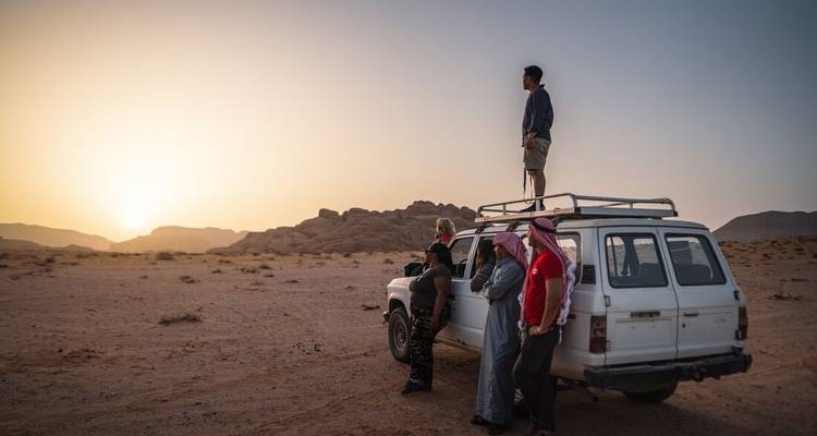 Four people by a jeep in a desert at sunset