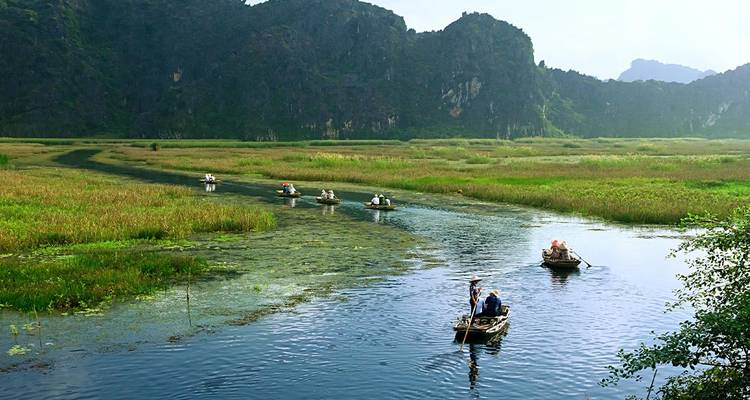 Boten op een rivier omringd door weelderig groen en kalkstenen bergen.