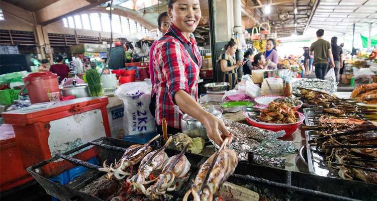 Een bruisende voedselmarkt met een vrouw die zeevruchten grilt.
