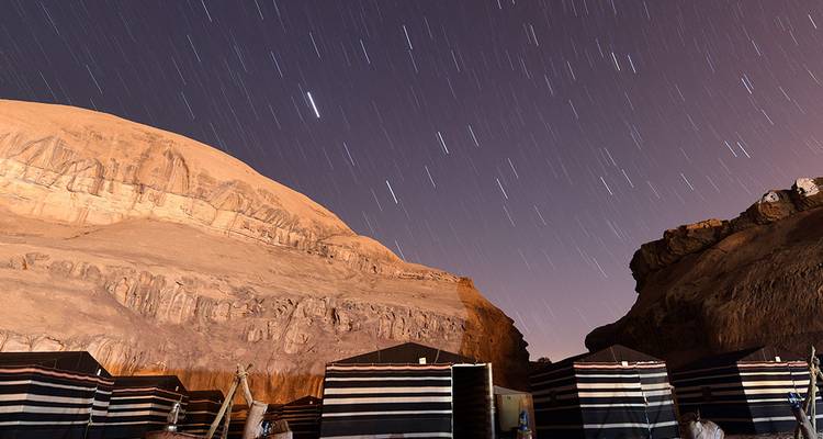 Ciel nocturne avec traînées d'étoiles au-dessus de tentes du désert.