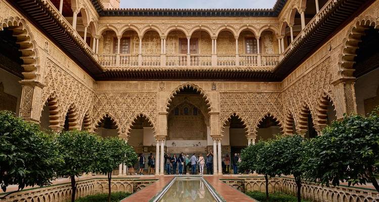 Les visiteurs admirent les arches mauresques et le bassin de réflexion dans la cour de l'Alcazar Royal de Séville.