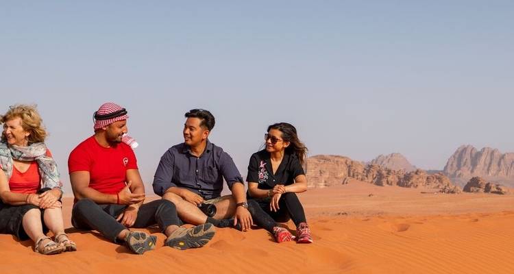 Group sitting on red desert sands with mountains.