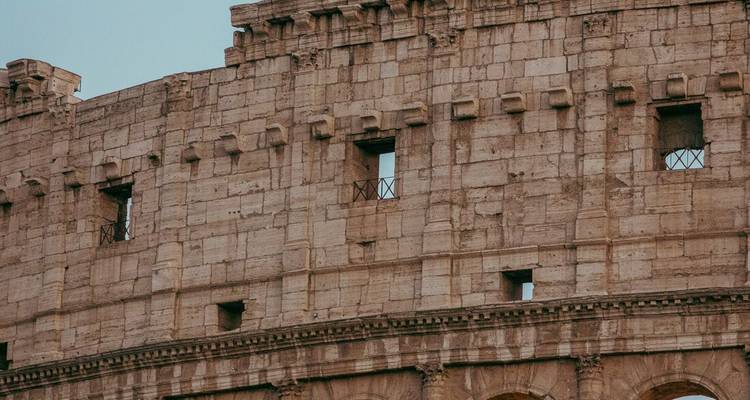 Gros plan sur les murs de pierre anciens et les arches du Colisée sous un ciel dégagé.