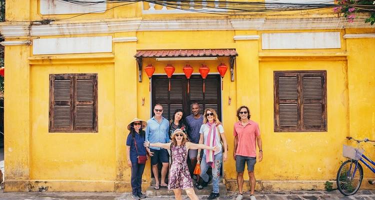 Group of tourists posing in front of a yellow historic building with lanterns.