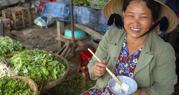 Woman smiling and eating in a vibrant market scene.
