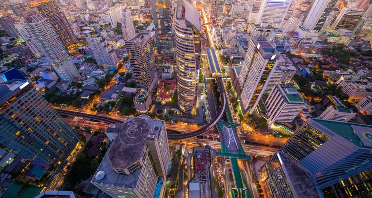 High-altitude aerial of Bangkok’s glittering skyscrapers and neon-lit highways at twilight.