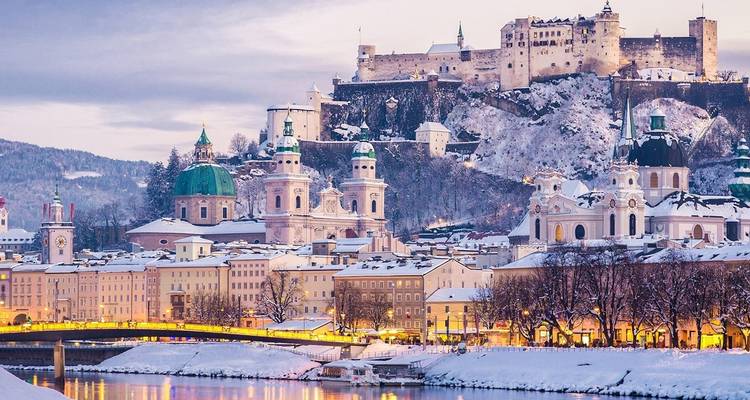 Besneeuwde skyline van Salzburg met barokke koepels en Burcht Hohensalzburg die gloeien bij schemering.