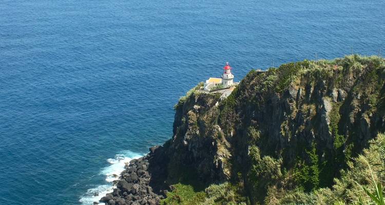 Phare au sommet rouge perché sur une falaise verte escarpée au-dessus de l'Atlantique bleu profond.