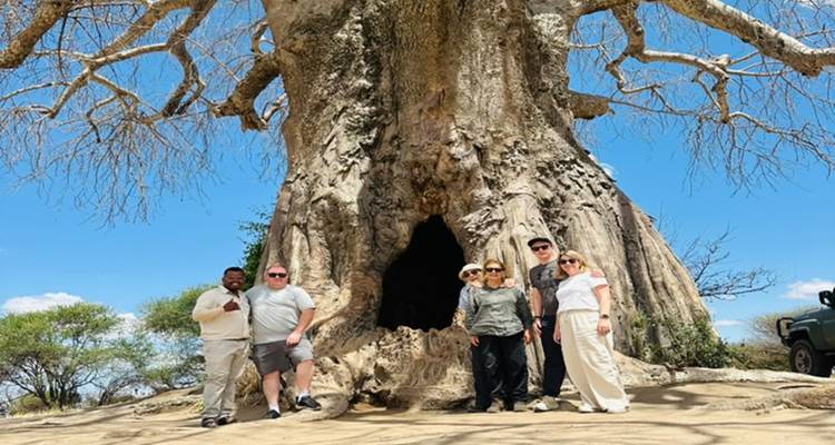 Los viajeros están de pie en la base de un enorme árbol baobab con una abertura de tronco hueco.