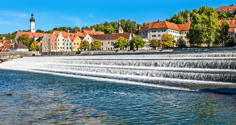 Cascade d'eau sur une rivière avec des bâtiments en arrière-plan.