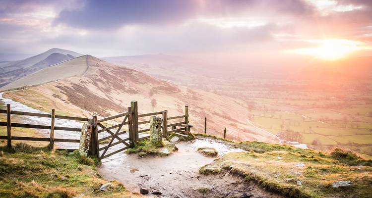 Zonsondergang over glooiende heuvels met een houten hek op de voorgrond.