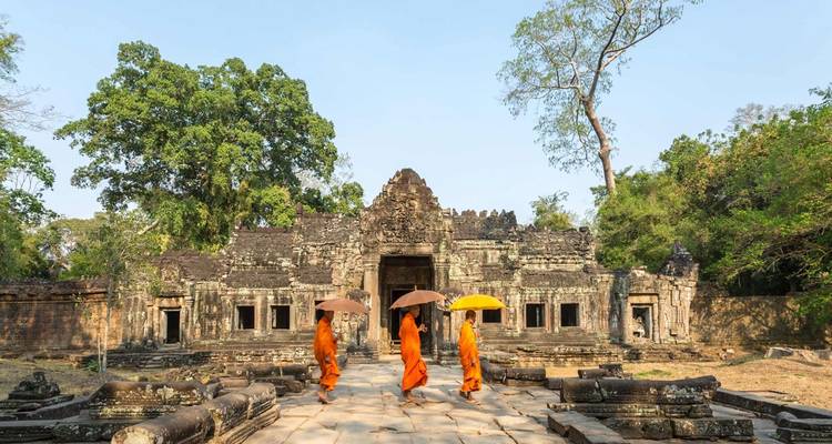 Des moines en robes orange marchant devant un ancien temple de pierre.