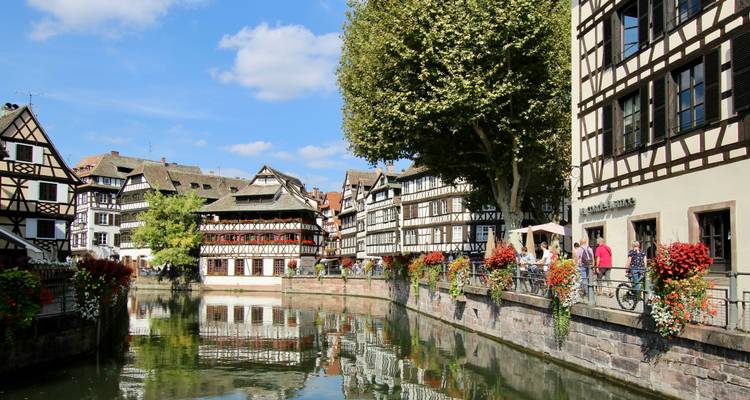 Casas con entramado de madera y coloridas jardineras reflejadas en un tranquilo canal en el barrio Petite France de Estrasburgo.