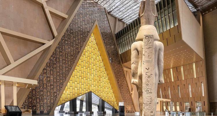 Intérieur de musée avec des statues et des motifs muraux en forme de pyramide.