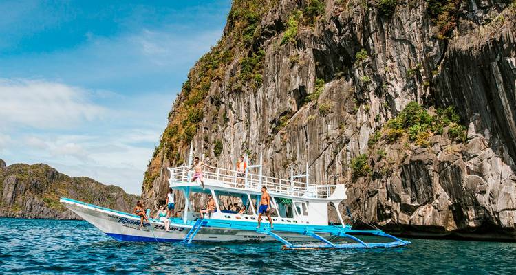 Un bateau bangka traditionnel avec des touristes près d'une île rocheuse.