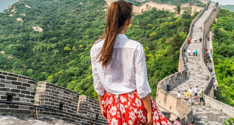 Una joven mira hacia la sinuosa Gran Muralla de China extendiéndose a través de colinas verdes.